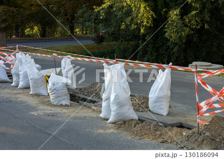 Construction work is taking place on the road, with sandbags and safety barriers in place to guide vehicles around the site during the afternoon Construction work is taking place on the road, with sandbags and safety barriers in place to guide vehicles around the site during the afternoon 130186094