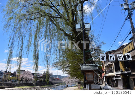 日本の岐阜県の高山市　中心部を流れる宮川と観光名所の宮川朝市　満開の桜と美しい青空　お昼過ぎの様子 130186543