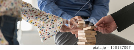 Wide view image of three business people making a tower of wooden pegs 130187097