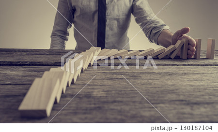 Businessman preventing dominoes from crumbling with palm 130187104