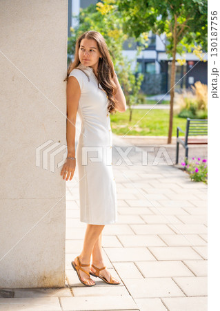 Young woman wearing a white midi dress walking outdoors in Old Money style. Concept of timeless fashion, graceful femininity and understated elegance in modern lifestyle. 130187756