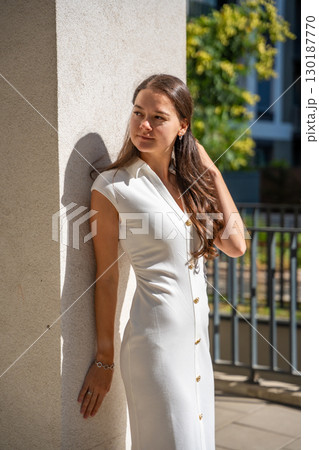 Young woman wearing a white midi dress walking outdoors in Old Money style. Concept of timeless fashion, graceful femininity and understated elegance in modern lifestyle. 130187770