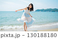 夏の海辺ではしゃぐ日本人女性｜白と水色のワンピースが風になびく爽やかな笑顔のポートレート 130188180