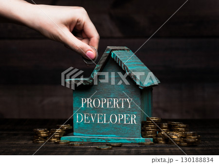 Wooden house model with coins next to it and hand 130188834