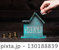 Wooden house model with coins next to it and hand 130188839