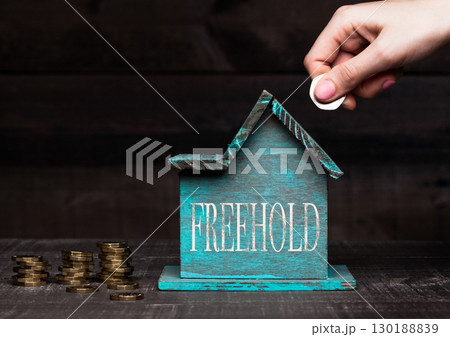 Wooden house model with coins next to it and hand 130188839