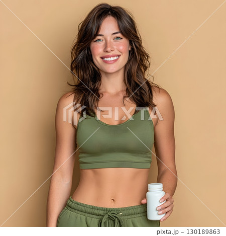 Smiling woman in green fitness clothes holds a white bottle. She represents healthy living and daily wellness for vitality. Smiling woman in green fitness clothes holds a white bottle. She represents healthy living and daily wellness for vitality. 130189863