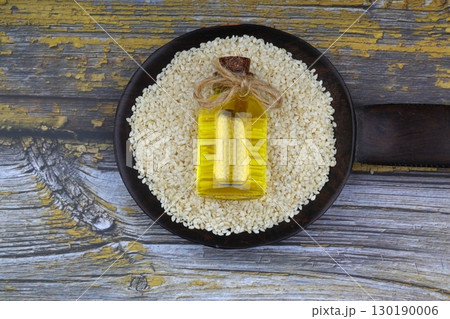 Glass bottle of sesame oil and raw sesame seeds in wooden spoon or bowl on rustic table. Uncooked sesame background concept with copy space Glass bottle of sesame oil and raw sesame seeds in wooden spoon or bowl on rustic table. Uncooked sesame background concept with copy space 130190006