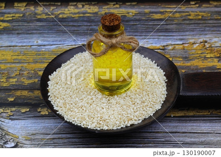 Glass bottle of sesame oil and raw sesame seeds in wooden spoon or bowl on rustic table. Uncooked sesame background concept with copy space Glass bottle of sesame oil and raw sesame seeds in wooden spoon or bowl on rustic table. Uncooked sesame background concept with copy space 130190007