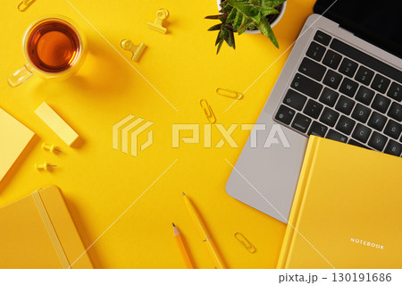 Yellow workspace with laptop, notebook, tea, plant, and stationery. Top view, space for your text. Yellow workspace with laptop, notebook, tea, plant, and stationery. Top view, space for your text. 130191686