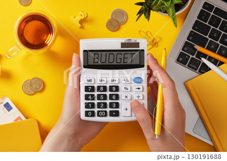 Hands holding calculator with word budget on screen. Money, laptop, and yellow stationery. Finance and business concept with copyspace. 130191688