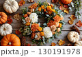 Thanksgiving wreath adorned with orange and white flowers, pumpkins, and autumn leaves in a festive setting 130191978
