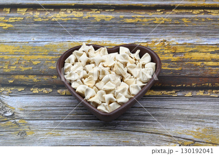 handmade manti (turkish ravioli type dumplings) on wooden heart shape bowl, before cooking 130192041