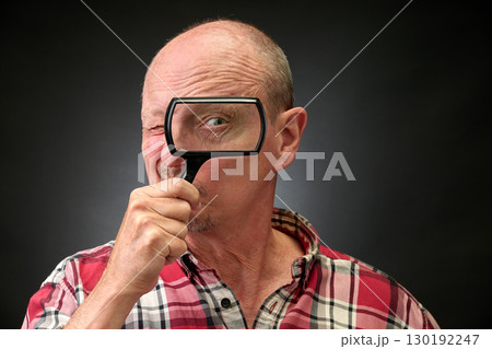 Closeup portrait of a elderly man in studio using a magnifying glass 130192247