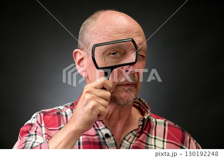 Closeup portrait of a elderly man in studio using a magnifying glass Closeup portrait of a elderly man in studio using a magnifying glass 130192248