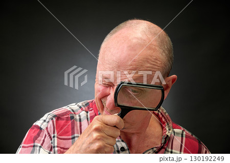 Closeup portrait of a elderly man in studio using a magnifying glass Closeup portrait of a elderly man in studio using a magnifying glass 130192249