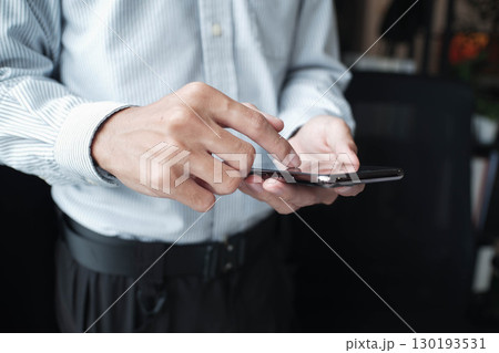 Closed-up hand of businessman using mobile phone standing near window. 130193531