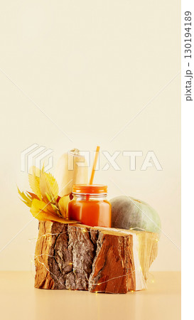 Autumn vertical composition with a glass of pumpkin juice with straw placed on a wooden platform near the pumpkins with autumn leaves and copy space. Healthy vegan drink, smoothies. Thanksgiving day 130194189