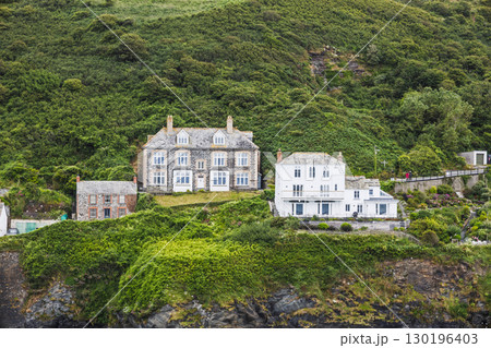 Clifftop coastal houses on lush green hillside, rugged shoreline village, scenic UK coast 130196403