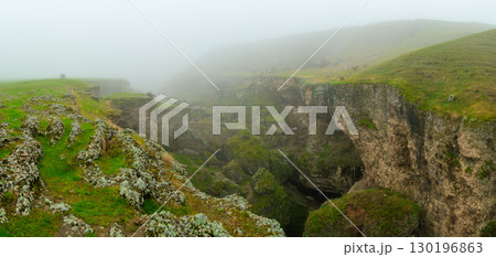 Rock formations and cracks covered with green moss in a misty landscape 130196863