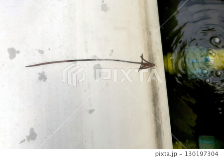 Pipe With Directional Arrow Positioned Above Calm Water Surface With Floating Objects Nearby Pipe With Directional Arrow Positioned Above Calm Water Surface With Floating Objects Nearby 130197304