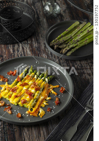 Delicious baked asparagus with melted cheese and bacon bits on a dark plate 130197752