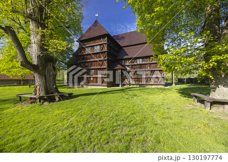 Wooden Church of Hronsek, Slovakia, bathed in sunlight with lush green grass and trees 130197774