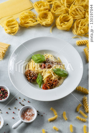 Delicious spaghetti bolognese with basil leaves and parmesan, surrounded by various types of pasta and spices 130197844