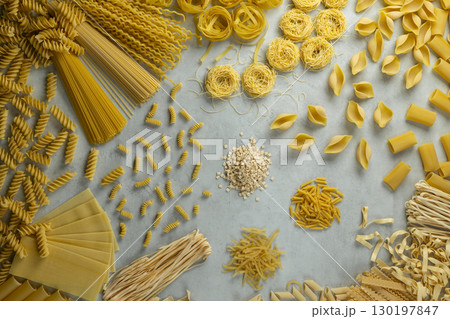 Variety of uncooked pasta shapes laying on gray background Variety of uncooked pasta shapes laying on gray background 130197847