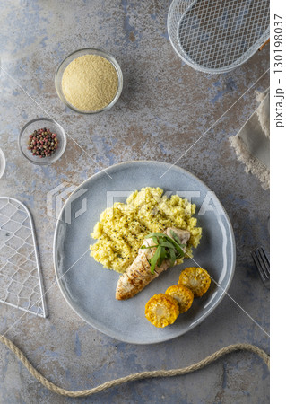 Grilled chicken breast with corn and aromatic couscous, ingredients and kitchen utensils surrounding plate Grilled chicken breast with corn and aromatic couscous, ingredients and kitchen utensils surrounding plate 130198037