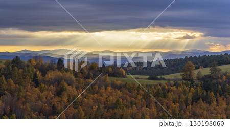 Sun rays shining through clouds over colorful autumn forest landscape with Low Tatras 130198060