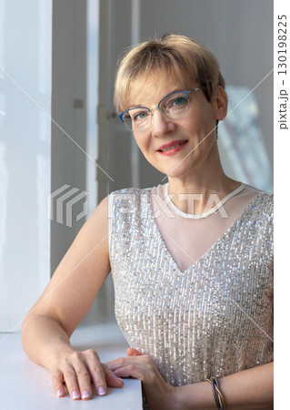 Portrait of smiling woman in festive clothes against a gray wall in a bright sunny room. Vertical photo. High quality photo 130198225