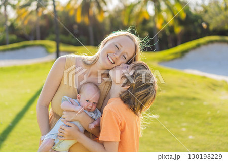Mother, older son, and newborn baby on a meadow in the park. Family spending quality time together in nature. Parenthood, love, and family bond concept Mother, older son, and newborn baby on a meadow in the park. Family spending quality time together in nature. Parenthood, love, and family bond concept 130198229