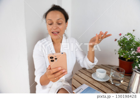 Woman Relaxing with Smartphone During Morning Coffee on Patio Woman Relaxing with Smartphone During Morning Coffee on Patio 130198428