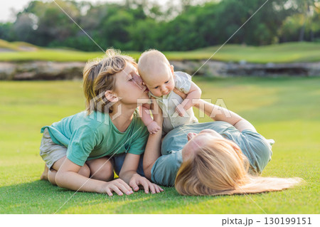 Mother, older son, and newborn baby on a meadow in the park. Family spending quality time together in nature. Parenthood, love, and family bond concept 130199151