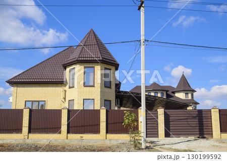 Decorative metal on the roof of a brick house. Fence made of corrugated metal. 130199592