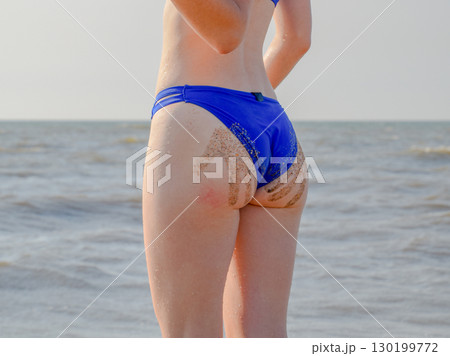 Woman in a blue swimsuit by the sea. A palm print in the form of sand on the priest at the woman 130199772