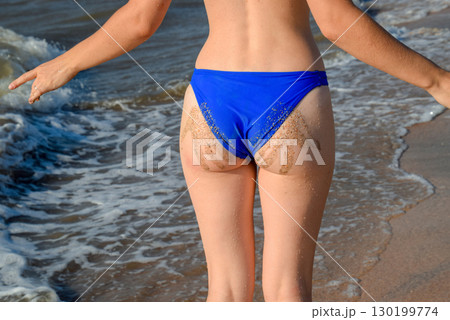 Woman in a blue swimsuit by the sea. A palm print in the form of sand on the priest at the woman 130199774