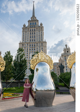 Woman in rose dress poses by mirrored matryoshka sculpture with golden ornament against the backdrop of the historic Radisson Royal Hotel Woman in rose dress poses by mirrored matryoshka sculpture with golden ornament against the backdrop of the historic Radisson Royal Hotel 130200822