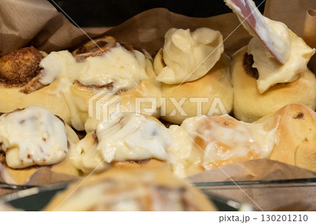 Woman spreading tasty cream onto baked cinnamon rolls on table in kitchen Woman spreading tasty cream onto baked cinnamon rolls on table in kitchen 130201210