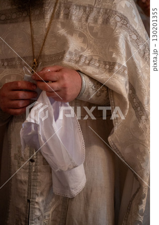 Close-up of an Orthodox priest preparing a white christening garment during a baptism ceremony Close-up of an Orthodox priest preparing a white christening garment during a baptism ceremony 130201355