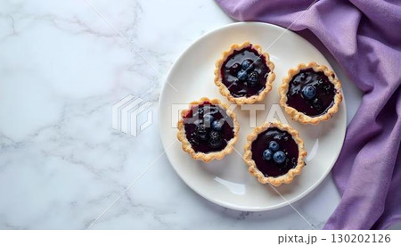 Four vibrant mini blueberry tarts on a white plate, celebrating the flavors of spring Four vibrant mini blueberry tarts on a white plate, celebrating the flavors of spring 130202126