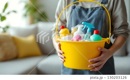 A woman holds a basket overflowing with cleaning supplies, reflecting her commitment to cleanliness and home maintenance 130203126