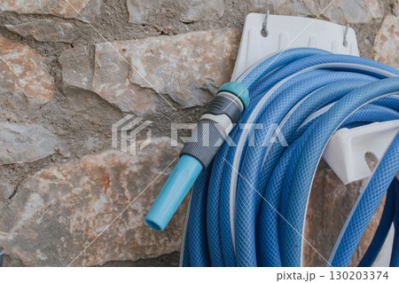 Garden hose with spray nozzle on holder by stone wall Garden hose with spray nozzle on holder by stone wall 130203374