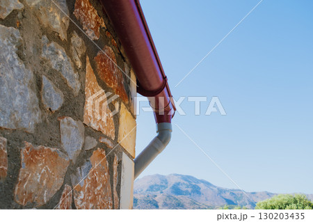 Rainwater drainage system of a building near a stone wall, designed to collect and divert precipitation from the roof 130203435