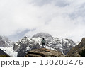 asian man standing on top of rock looking at peak of snow mountain 130203476