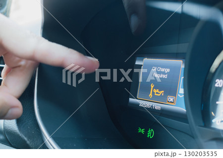 A male finger points to the oil change alert on a car dashboard display 130203535