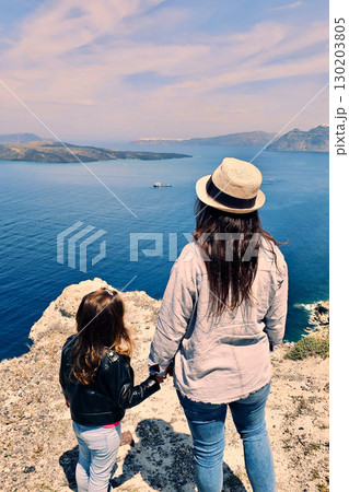 Mother and daughter looking at nearby island on a sunny spring day, Santorini, Greece 130203805