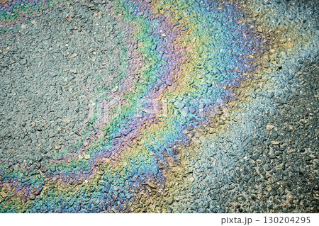 Rainbow oil slick on asphalt road creates colorful abstract pattern, highlighting environmental pollution. 130204295