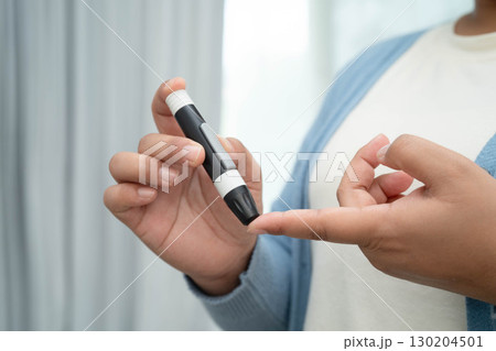 Asian woman self testing to check blood sugar level diabetes by digital lancet on finger at home. 130204501